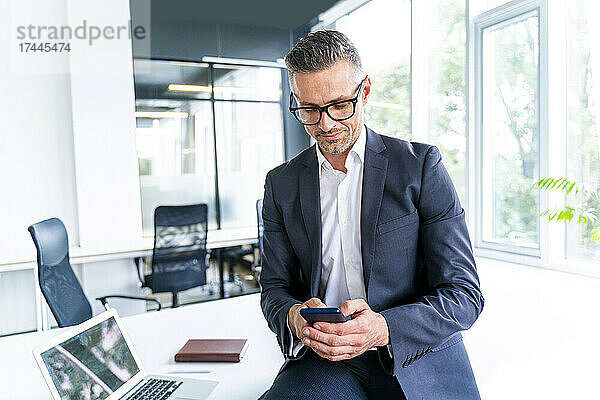 Männlicher Geschäftsprofi mit Brille und Smartphone im Büro