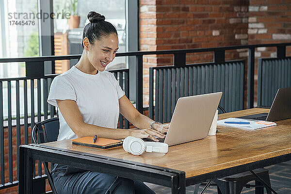 Lächelnde Berufstätige benutzt Laptop  während sie am Schreibtisch im Büro sitzt
