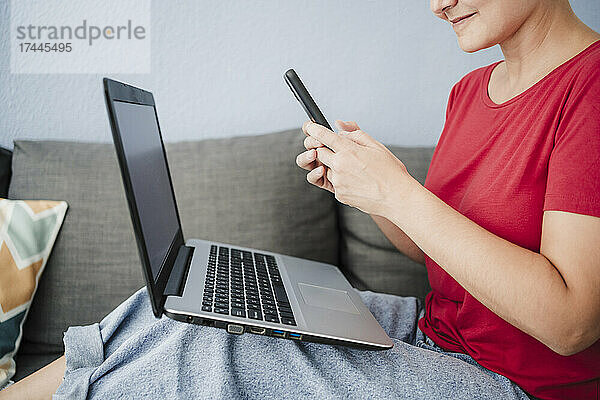 Freiberuflerin mit Laptop und Smartphone auf dem Sofa im Heimbüro
