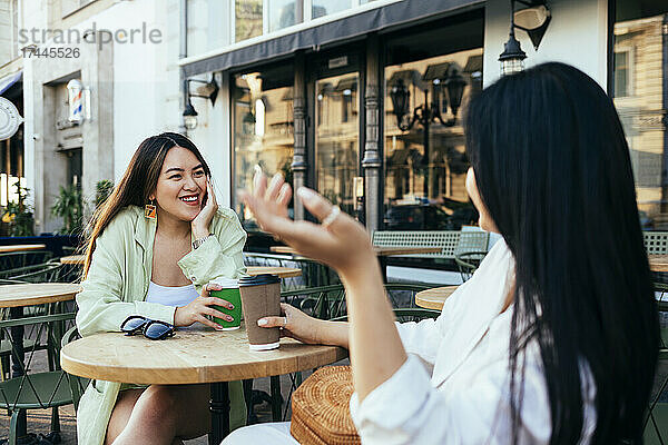 Freundinnen mit Kaffeetasse reden  während sie im Straßencafé sitzen