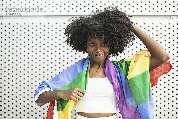 Afro-Frau mit Pride-Flagge steht vor einer Metallwand