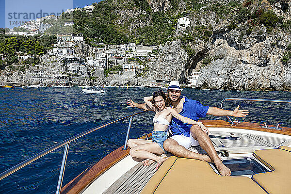 Lächelndes Paar mit ausgestreckten Armen sitzt im Motorboot