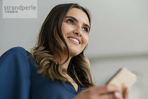 Lächelnde junge Geschäftsfrau mit Smartphone im Büro