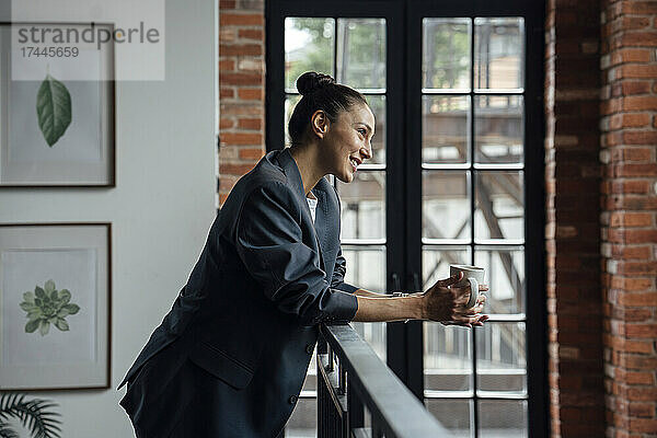 Lächelnde  nachdenkliche Geschäftsfrau mit Kaffeetasse im Büro