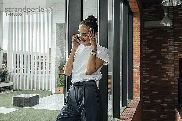 Lächelnde Geschäftsfrau mittleren Alters  die im Büro mit dem Mobiltelefon spricht