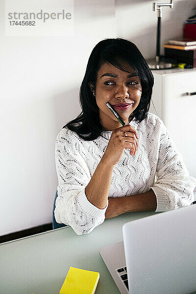 Nachdenkliche Geschäftsfrau mit Laptop sitzt im Heimbüro