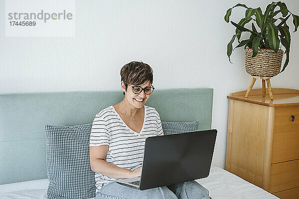 Lächelnde Frau benutzt Laptop zu Hause im Bett