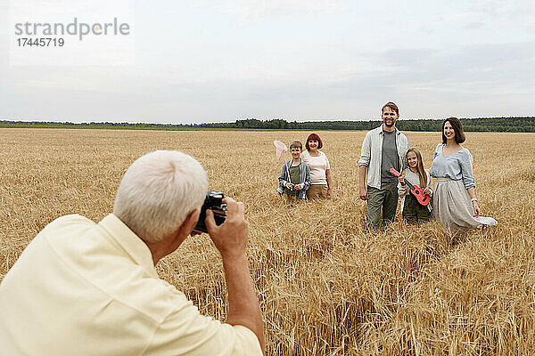 Mann fotografiert Familie mit Kamera auf Weizenfeld