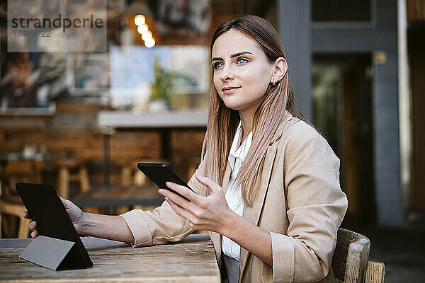 Geschäftsfrau mit Mobiltelefon und digitalem Tablet sitzt im Café