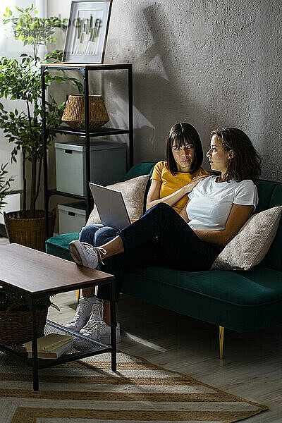 Lesbisches Paar mit Laptop redet  während es zu Hause auf dem Sofa sitzt