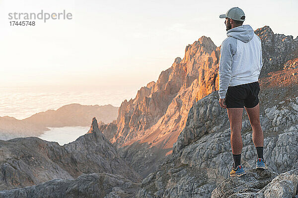 Männlicher Tourist blickt auf Berge  während er auf einem Felsen steht  Picos de Europe  Kantabrien  Spanien