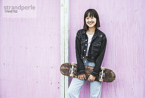 Glückliches Teenager-Mädchen hält Skateboard vor der Wand