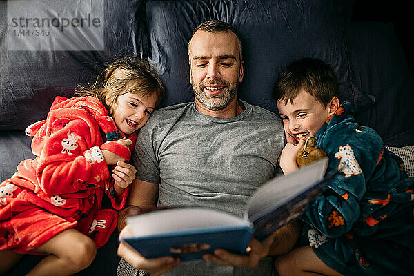 Vater liest seinen Kindern nachts im Hauptschlafzimmer ein Buch vor