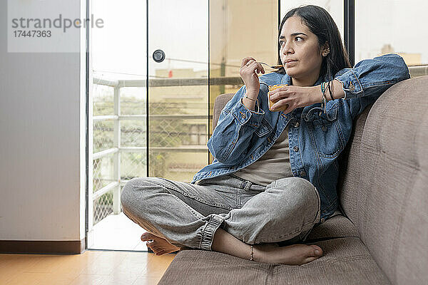 Frau isst hausgemachte Cashewbutter und sitzt auf einem Sofa