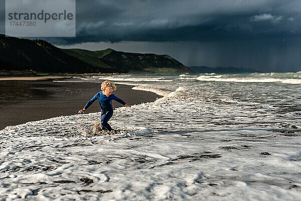 Fröhliches Kind spielt am Strand mit dramatischem Himmel im Hintergrund