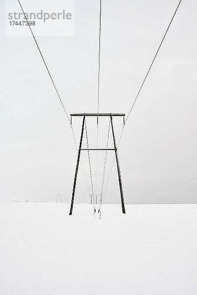 Sendemast mit Leitungen über verschneitem Gelände im Winter