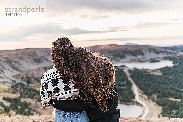 Rückansicht von zwei Frauen  die sich umarmen und neben einem See mit Bergen stehen