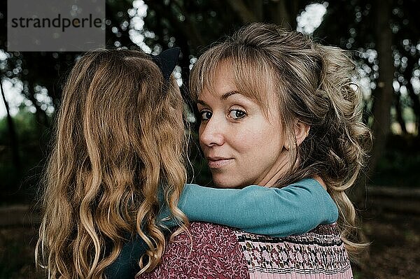 Porträt einer Mutter  die zurückblickt  während sie ihre Tochter hält