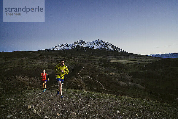 Ein Mann und eine Frau laufen im Morgengrauen mit Bergen in der Ferne