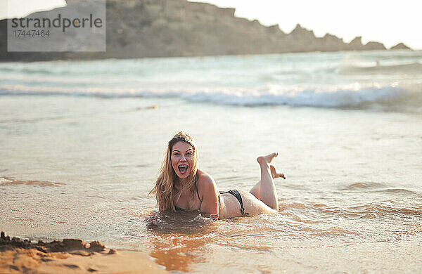 Lächelnde junge Frau  die am Strand liegt