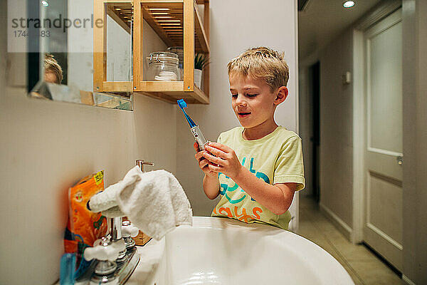 Junge putzt glücklich Zähne mit elektrischer Zahnbürste