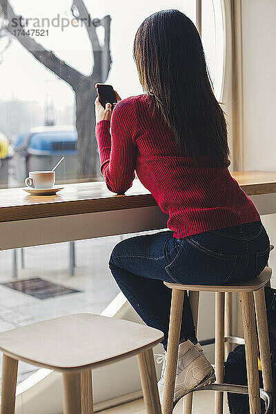 Mädchen tippt beim Kaffeetrinken eine Nachricht auf ihrem Mobiltelefon