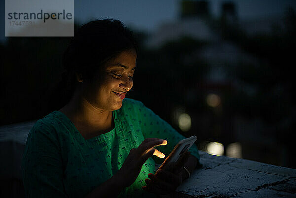 Junge Frau schaut in der blauen Stunde auf das Handy auf dem Dach