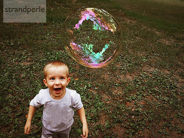 Fröhlicher Junge lächelt und schaut draußen auf die Seifenblase