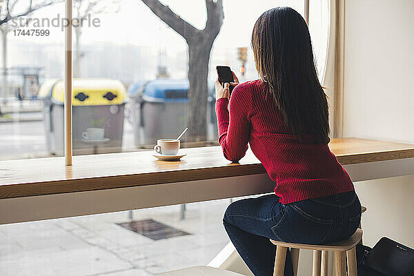 Mädchen tippt beim Kaffeetrinken eine Nachricht auf ihrem Mobiltelefon