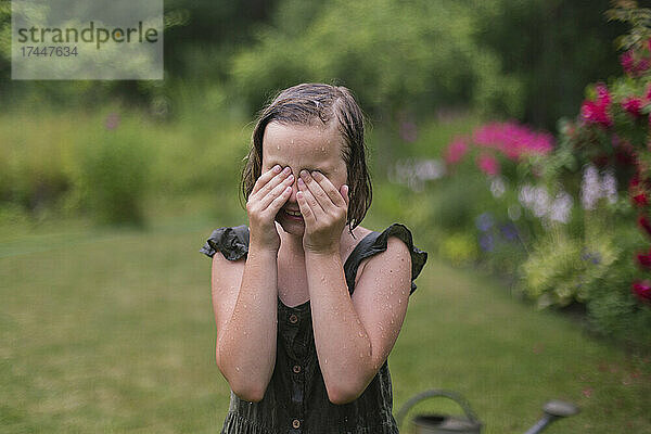 Mädchen im Regen wischt sich in ihrem Garten die Augen.