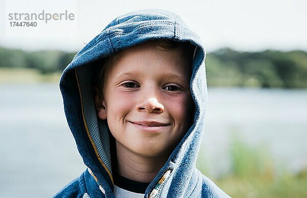 Porträt eines lächelnden Jungen mit Kapuze am Strand