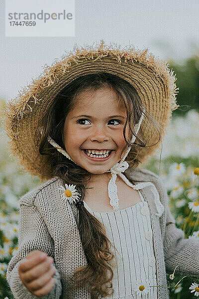 Ein Mädchen mit Hut lächelt vor dem Hintergrund eines Kamillenfeldes.