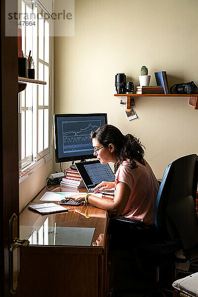 Weibliche Maklerin handelt an der Börse mit Laptop vom Heimbüro aus.