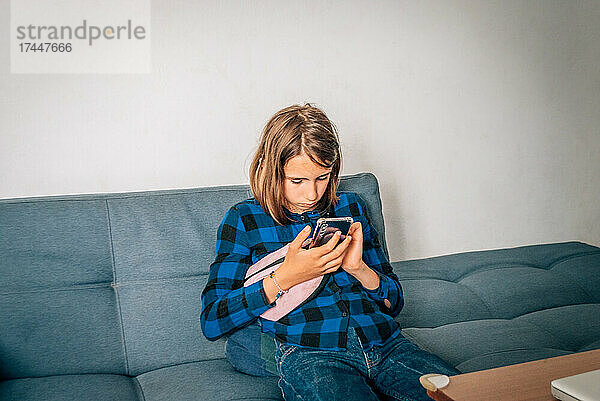Ein Mädchen sitzt zu Hause auf der Couch und hat ein Telefon in der Hand.