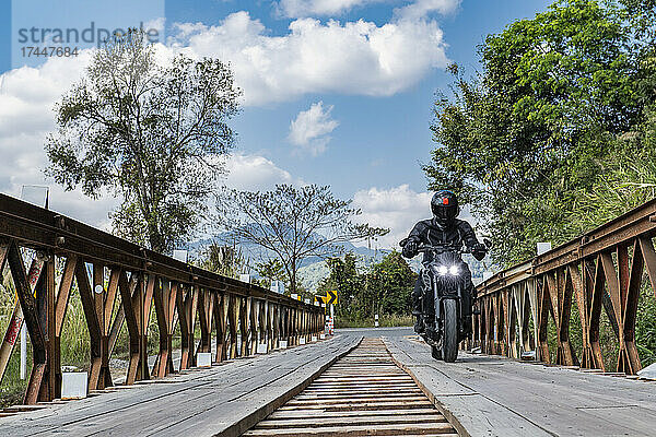 Mann fährt mit seinem Motorrad über eine Behelfsbrücke im Norden Thailands