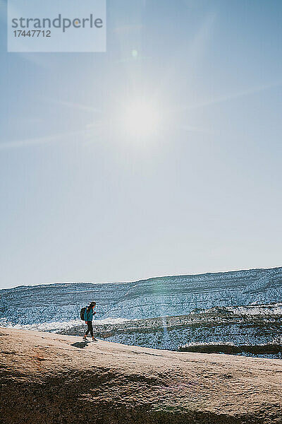 Eine Frau mit Krempenhut und Rucksack wandert allein in der Wüste
