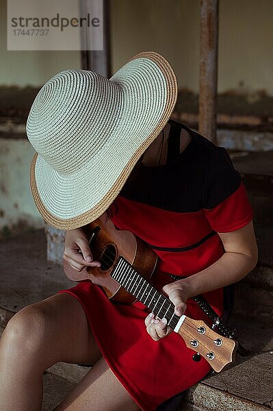 Side view of sitting girl in hat  playing ukulele  on old steps