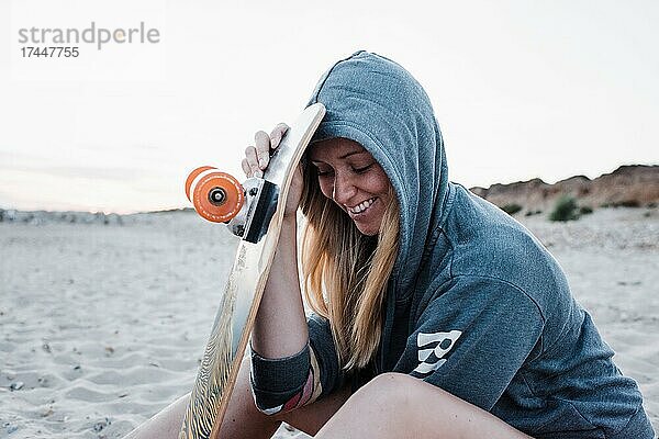 Porträt einer Frau  die lächelnd mit ihrem Skateboard am Strand saß