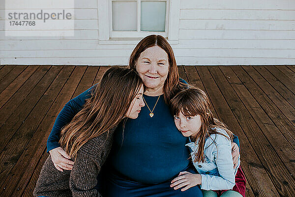 Oma und Enkelinnen umarmen sich auf der Veranda des Hauses