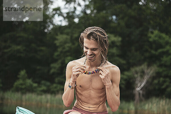 Gesunder Bohemien-Mann lacht mit bunter Halskette am natürlichen See