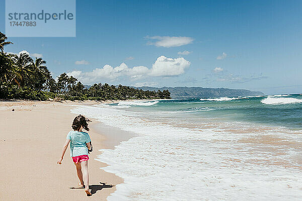 Junges Mädchen läuft im Sand neben dem Meer an einem Strand in Oahu