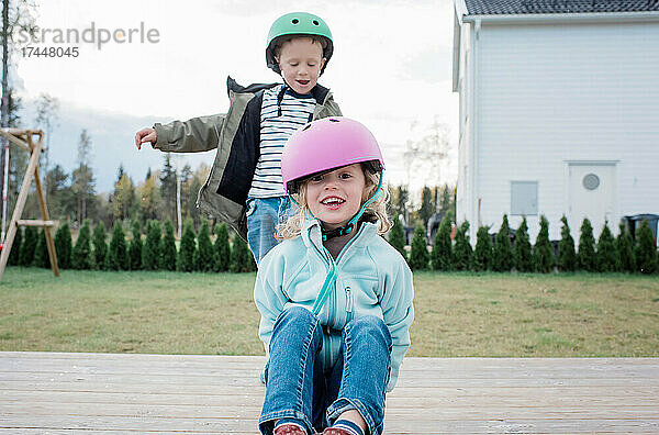 Bruder und Schwester spielen lachend auf einem Skateboard im Garten