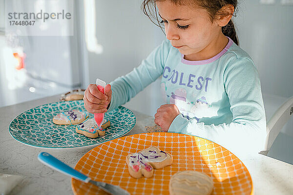 Kleines Mädchen dekoriert Osterplätzchen mit Zuckerguss