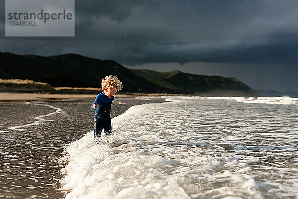 Lockiges Kind spielt in Wellen am Strand in Neuseeland