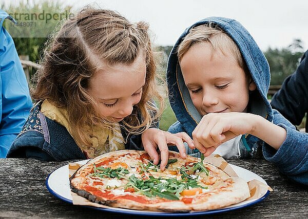 Mädchen und Junge teilen sich gemeinsam eine Pizza in einem Restaurant im Freien