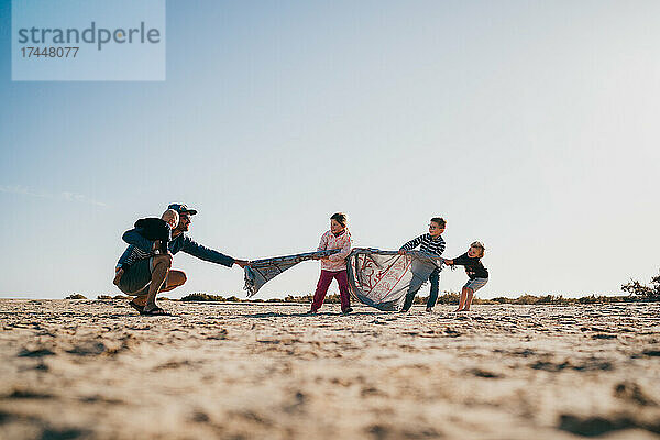 Papa und Kinder spielen mit Handtüchern am Strand und haben Spaß auf Fuerteventura