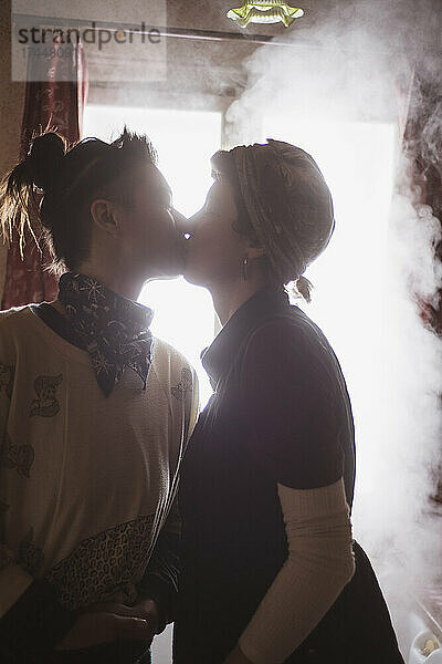 Queeres weibliches Paar küsst sich im dampfenden Fenster einer Küchenhütte in Tschechien