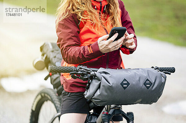 Frau genießt die Natur mit dem Mountainbike und nutzt ihr Smartphone