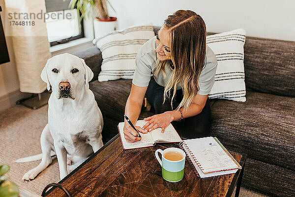 Frau schreibt in Notizbuch  während sie ihren Hund ansieht