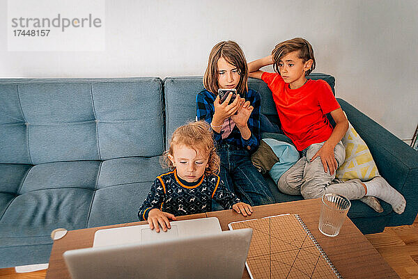 Drei Kinder schauen sich Zeichentrickfilme an und spielen auf Telefon und Laptop